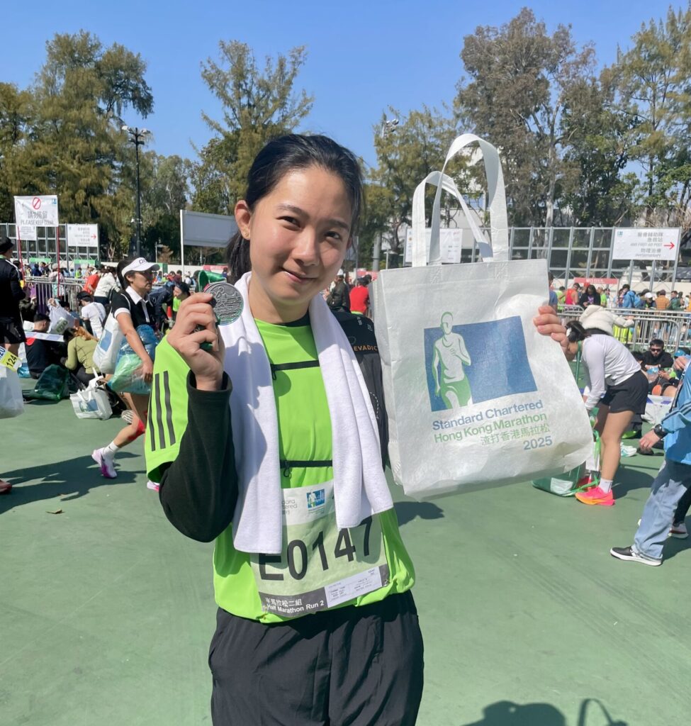A finisher holding a medal and an EzyGreenPak plant-based water-soluble nonwoven finisher bag at the Standard Chartered Hong Kong Marathon